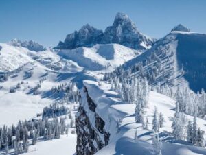 Snow-covered jagged mountain peaks with frosted evergreen trees under a clear blue sky.